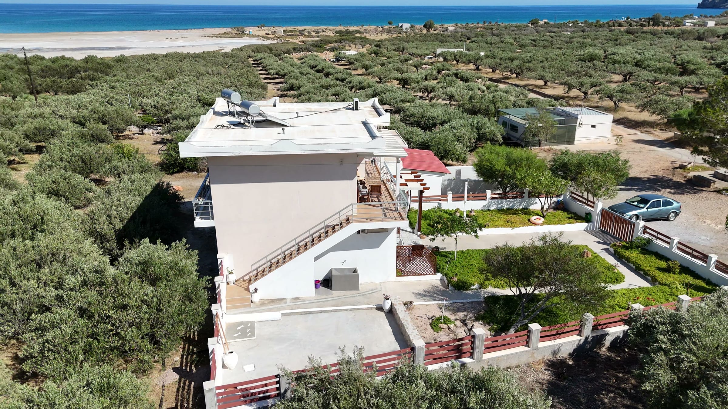 The house from the air, white against the olive groves, with the bay and the open sea behind it