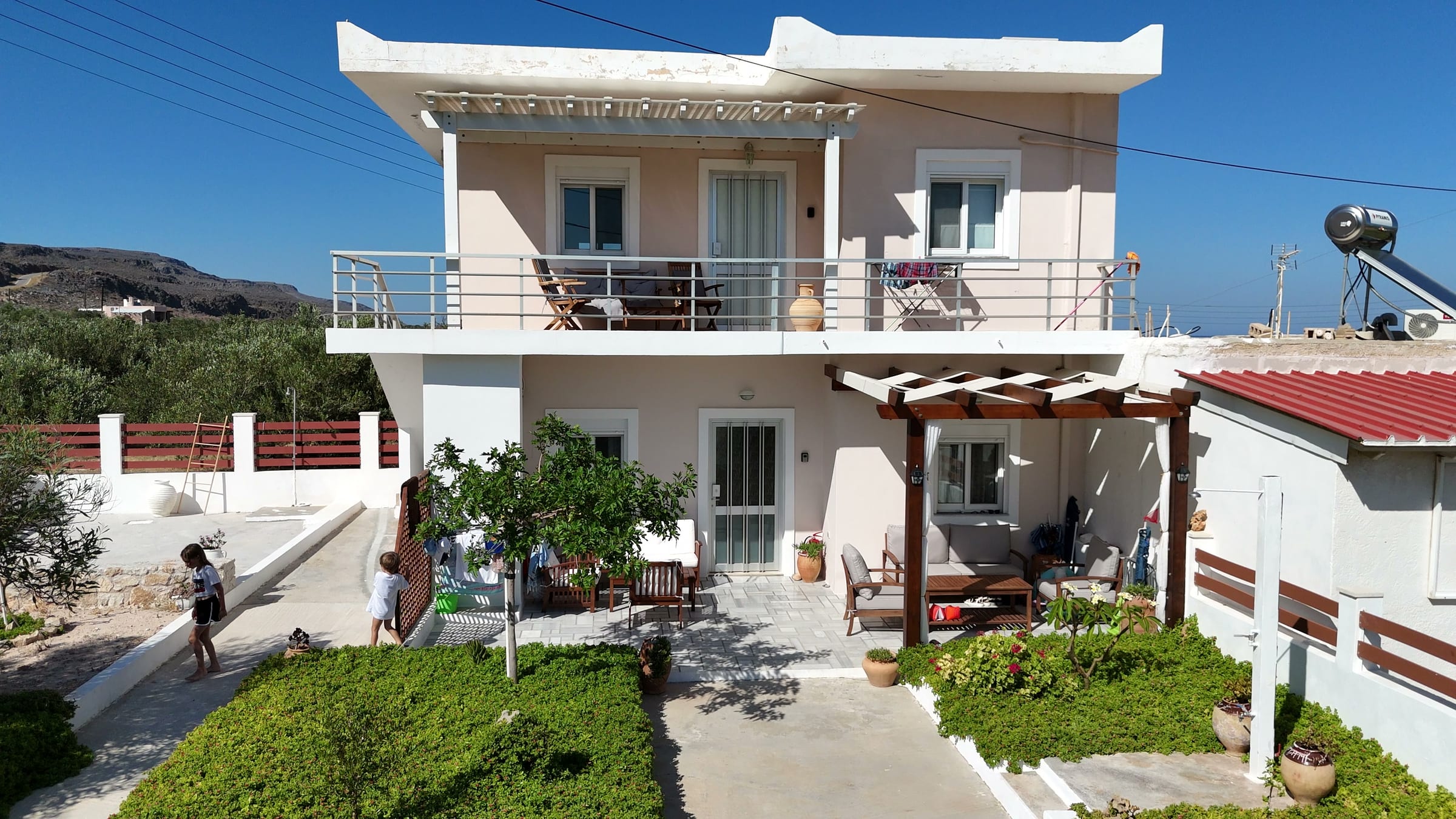 The front of the house, two storeys of whitewash with a balcony above and a pergola over the terrace below